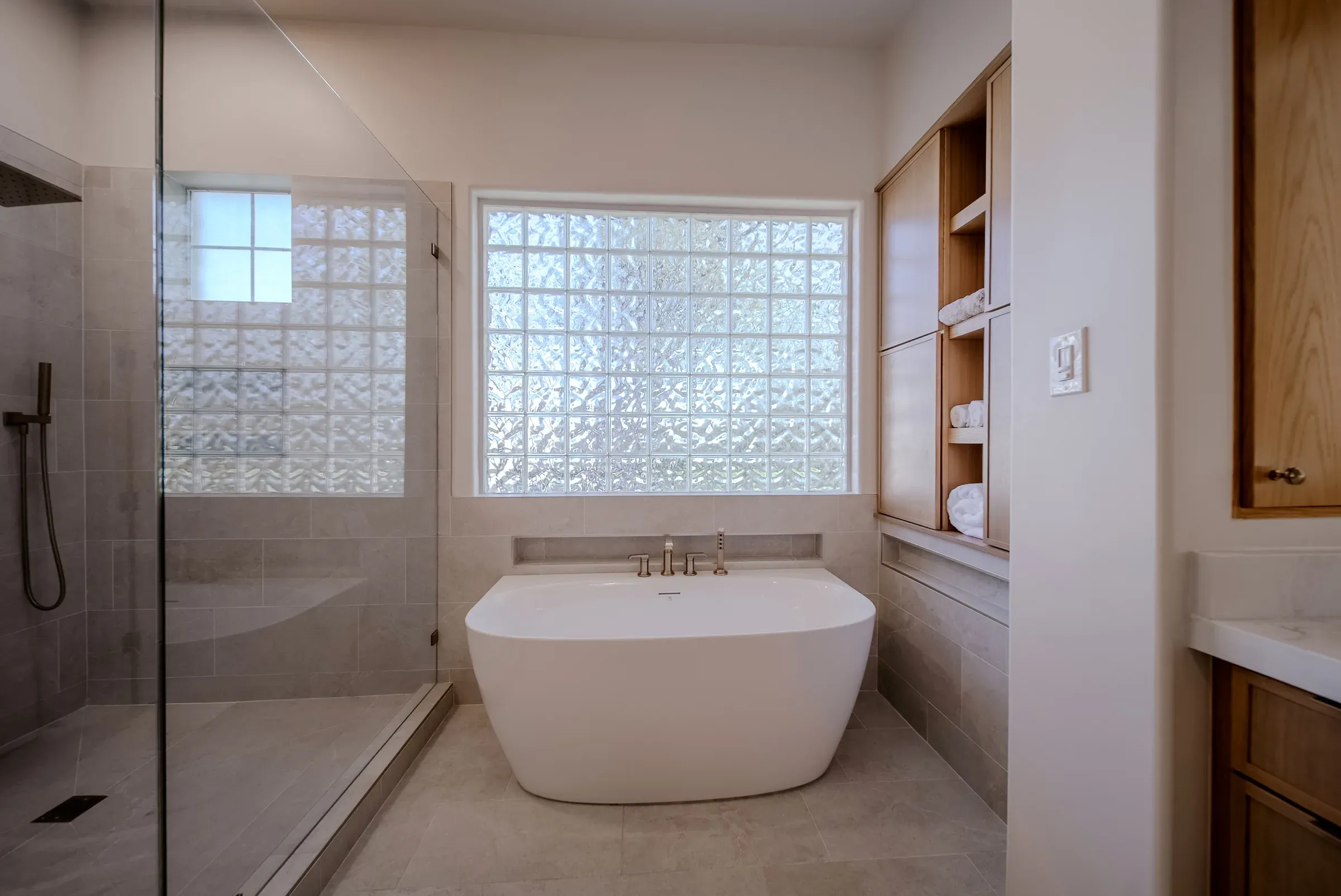 Remodeled Austin primary bathroom with a freestanding soaking tub, glass walk-in shower, and white oak built-in shelving