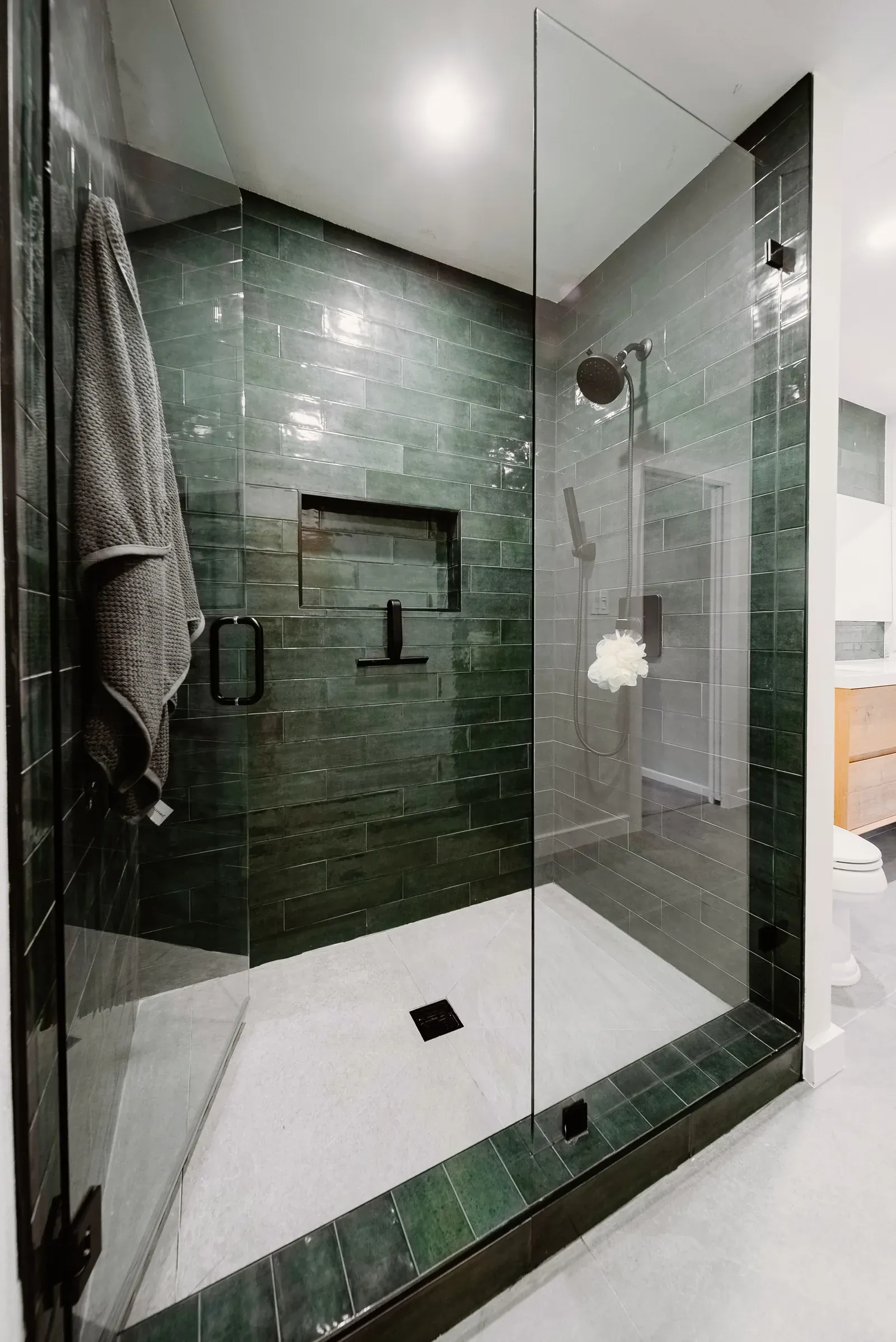 Finished walk-in shower with a glass enclosure, green tile, and black fixtures installed