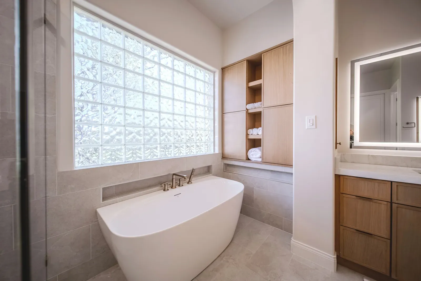 Freestanding soaking tub under a glass-block window in a remodeled Austin primary bathroom