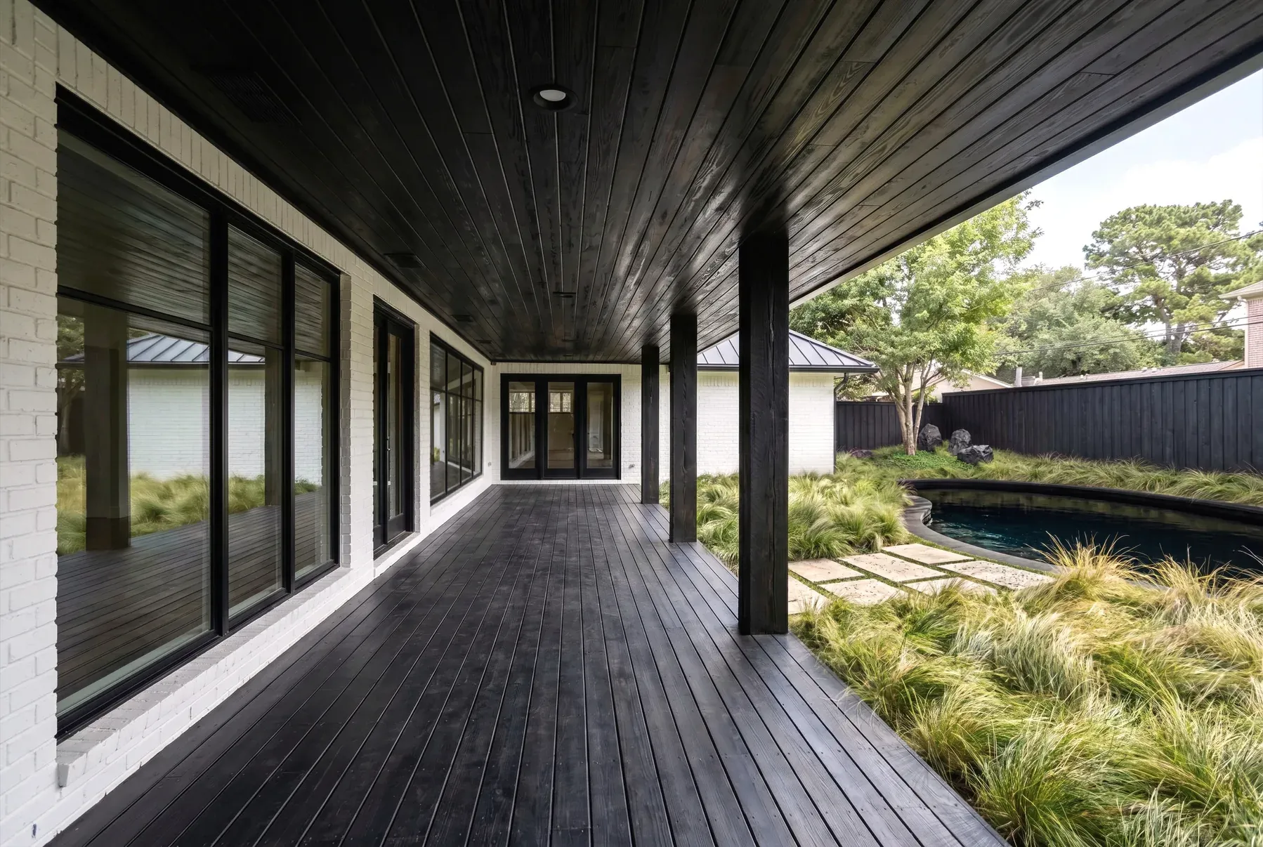 Covered deck clad in charred shou sugi ban wood beside a dark pool and prairie grass