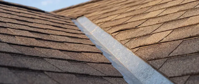 Two asphalt shingle roof planes meeting at a valley lined with metal flashing, in low evening sun