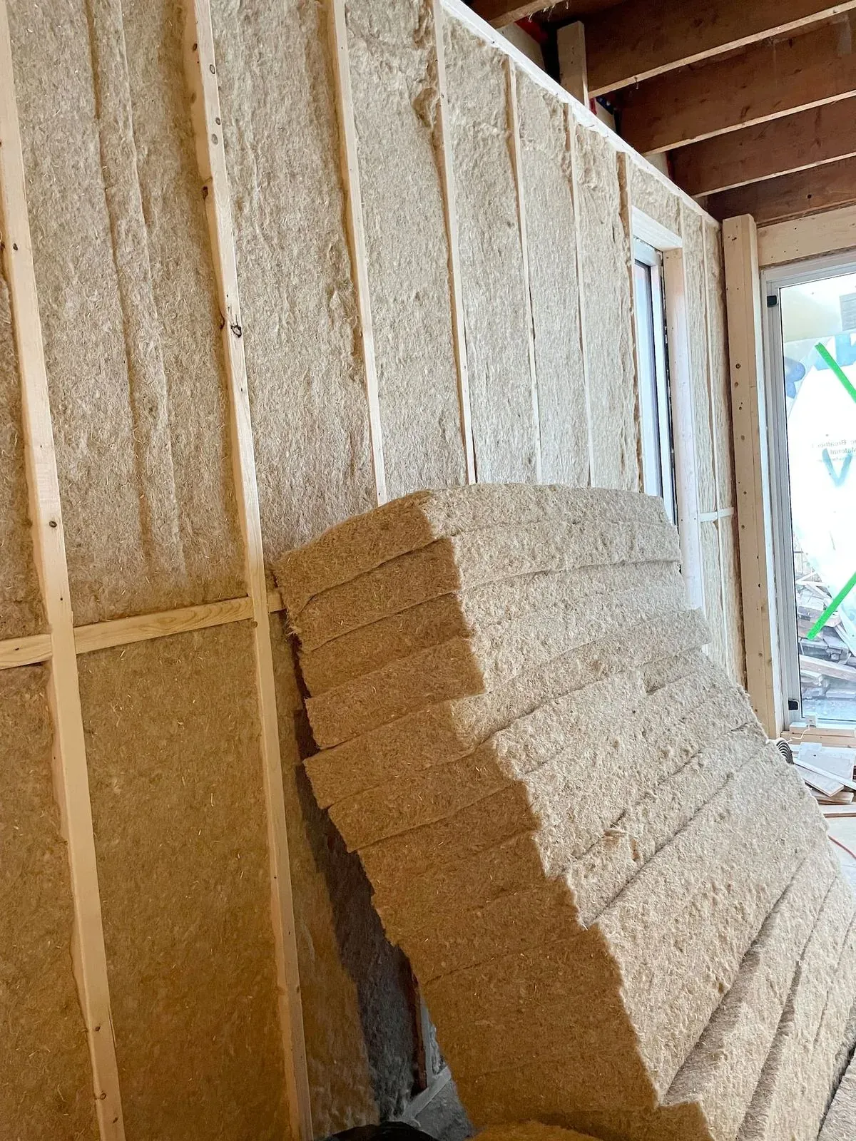 Natural fibre batt insulation stacked against wood stud framing on a job site