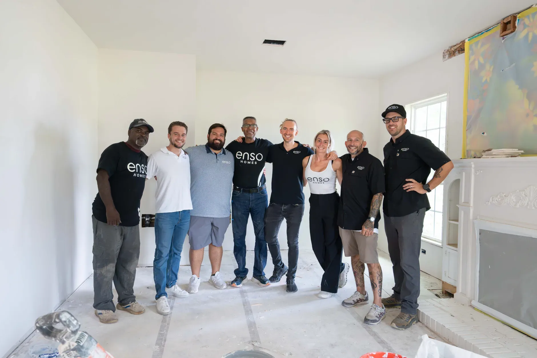 The Enso Homes team standing together in a house mid-remodel, drop cloths on the floor and the fireplace masked off